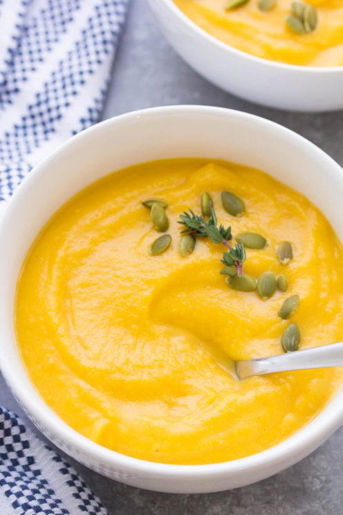 Butternut squash soup in a white bowl garnished with pepitas and thyme.