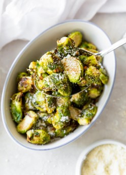air fryer brussels sprouts with parmesan on a serving spoon held over a serving dish