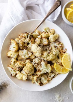 air fryer cauliflower in a bowl with lemon wedges and serving spoon