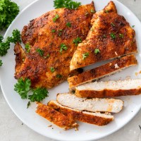 two seasoned air fryer chicken breasts on a plate with one breast partially sliced