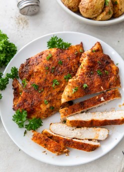 Two air fryer chicken breasts on a plate with one partially sliced.
