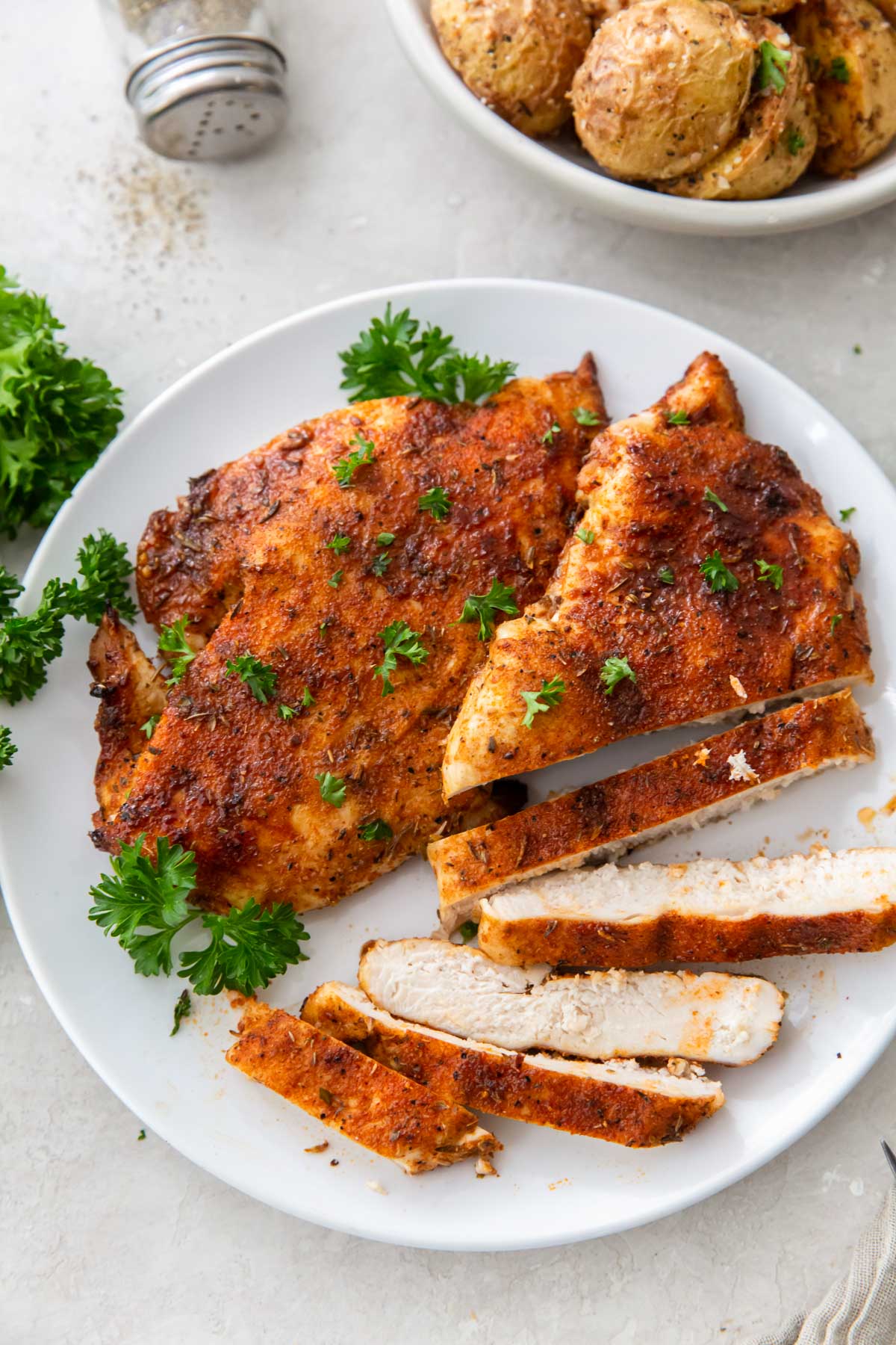 two air fryer chicken breasts on a plate with one partially sliced