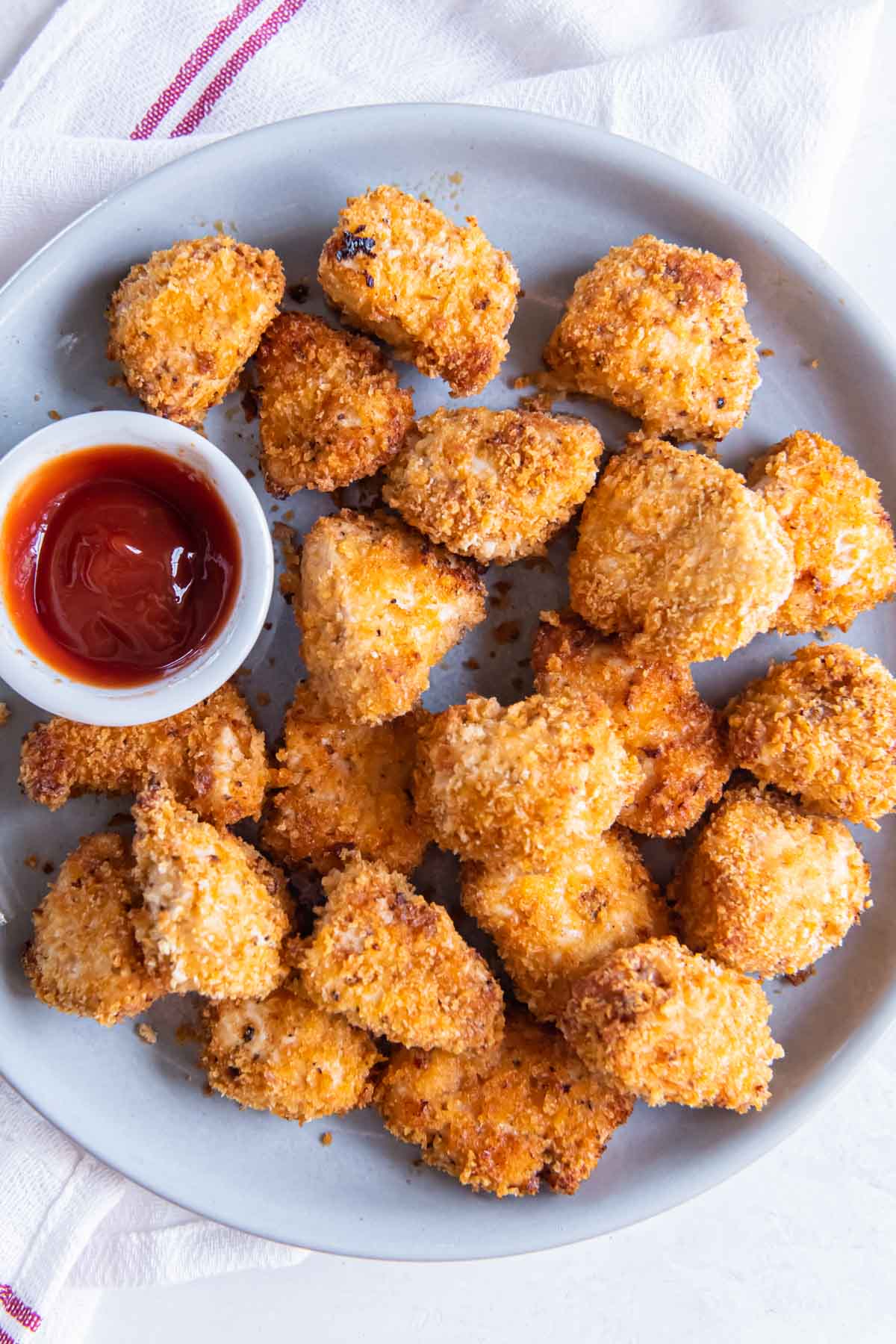 Air fryer chicken nuggets served on a plate with a small dish of ketchup.