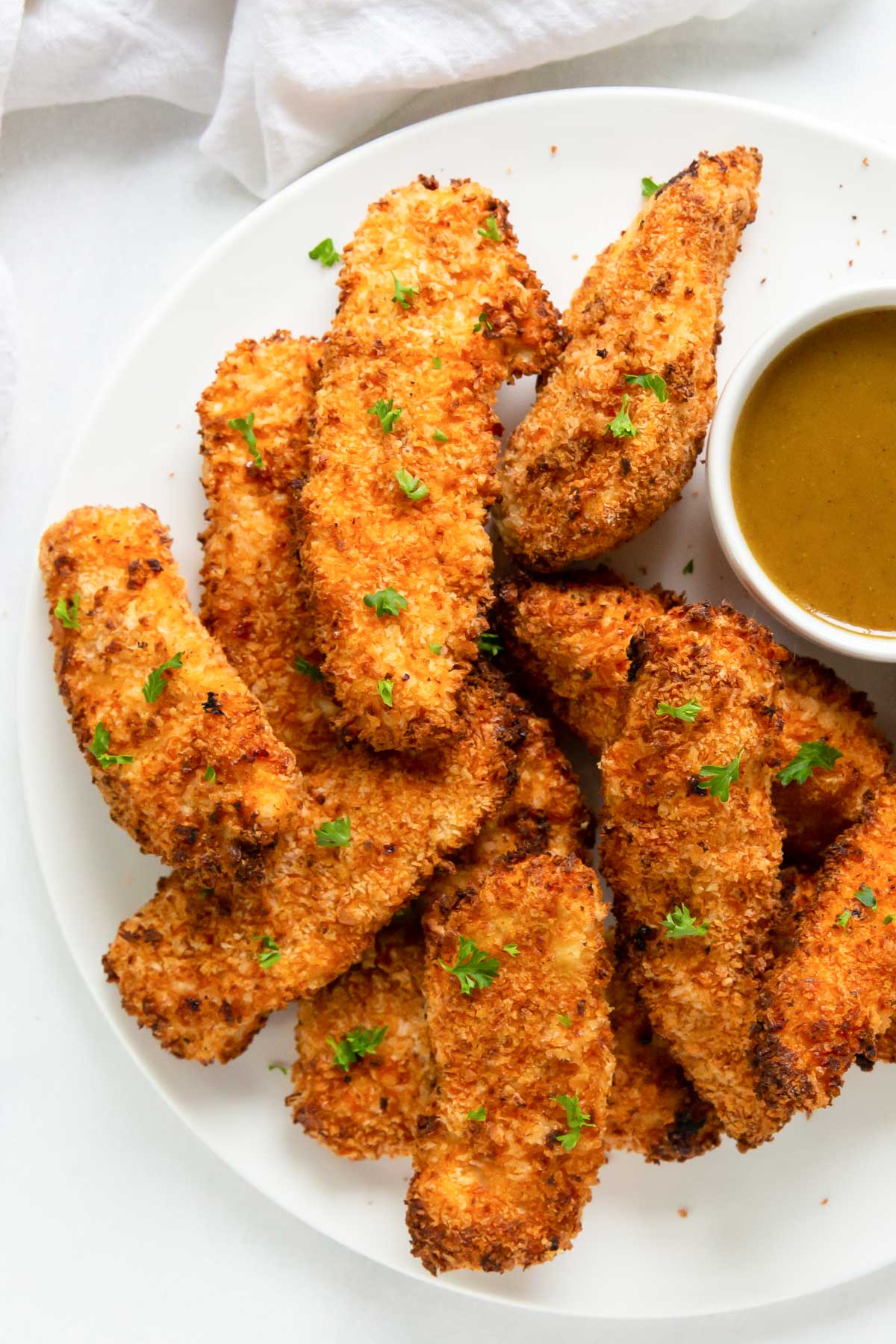 air fryer chicken tenders stacked on a plate with a dish of honey mustard sauce