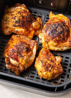 four cooked chicken thighs in air fryer basket