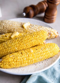 Four ears of corn on the cob on a plate with melty butter, salt and pepper.