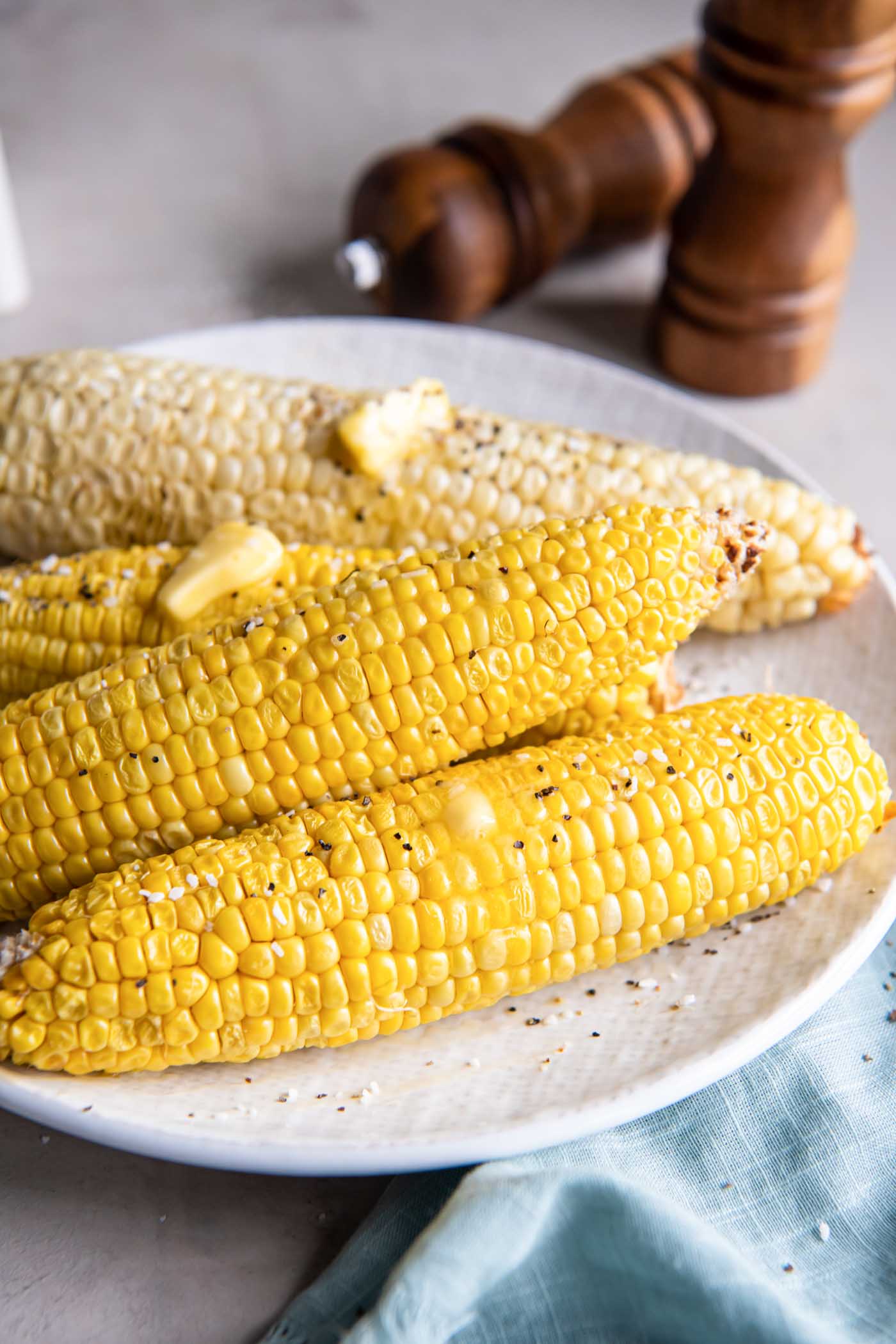 Four ears of corn on the cob on a plate with melty butter, salt and pepper.