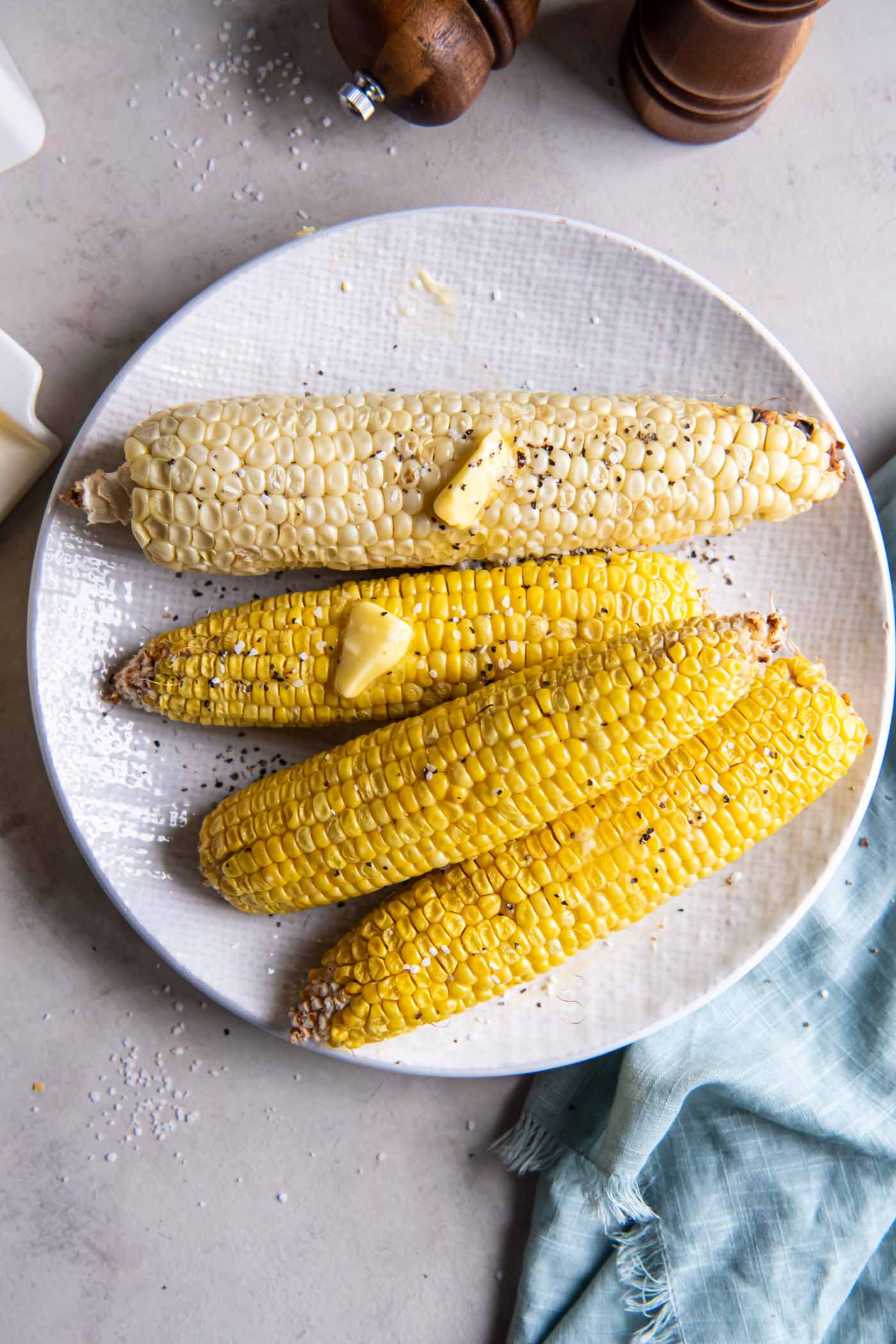 Four ears of corn on a plate with butter, salt and pepper.