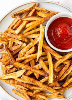 a plate of air fryer french fries with a small dish of ketchup