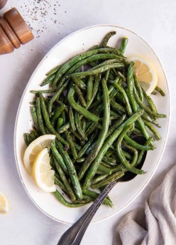 Air fryer green beans on an oval serving plate with lemon wedges and a serving spoon.