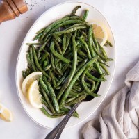 Air fryer green beans on an oval serving plate with lemon wedges and a serving spoon.