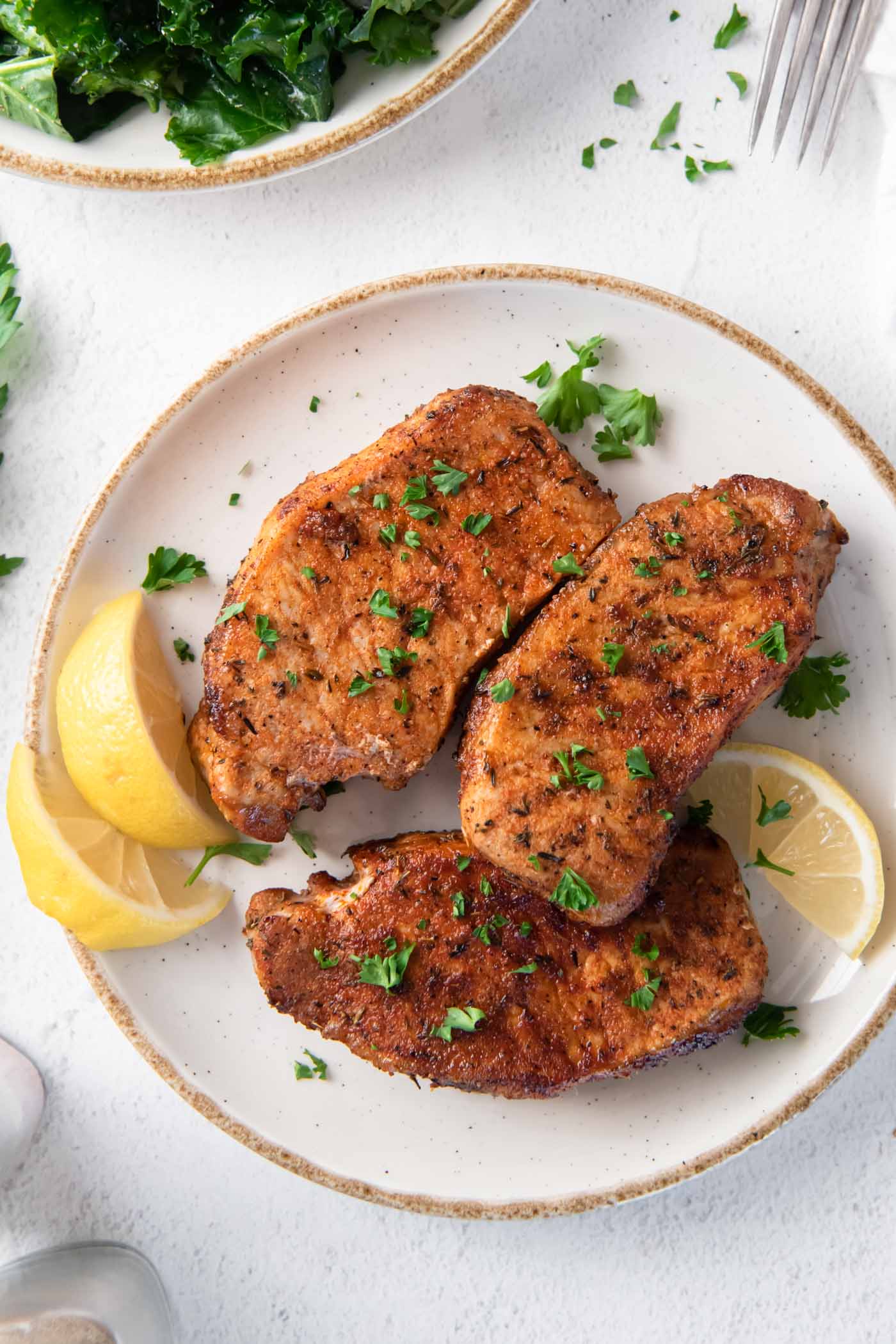 Three air fryer pork chops on a plate with parsley and lemon garnish.