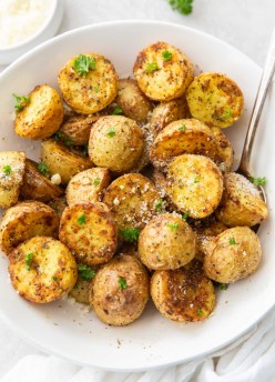 air fryer potatoes with parmesan in a white bowl with serving spoon