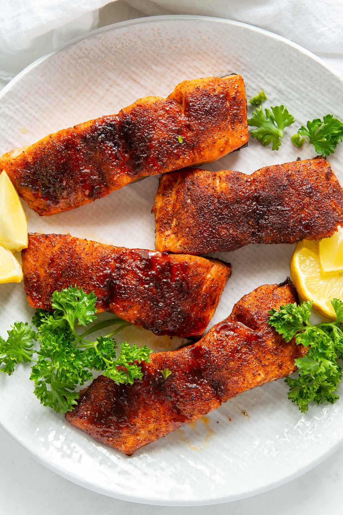 four air fried salmon fillets on a plate with parsley and lemon slices