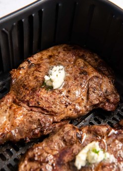 two cooked steaks in air fryer topped with pat of garlic butter