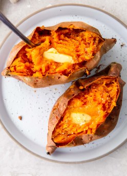Two air fryer baked sweet potatoes served with butter, salt and pepper.
