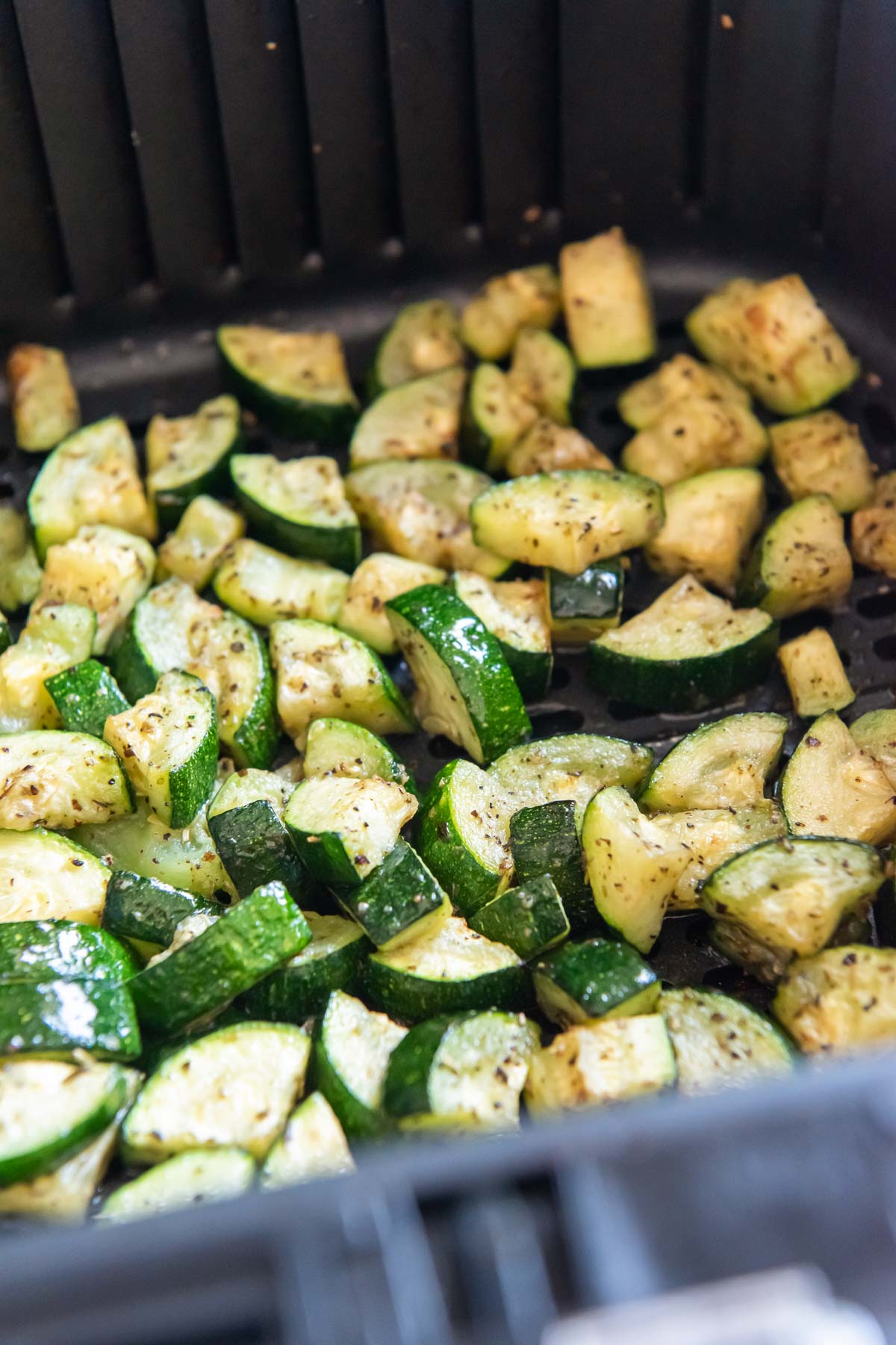 Cooked zucchini pieces in air fryer basket.