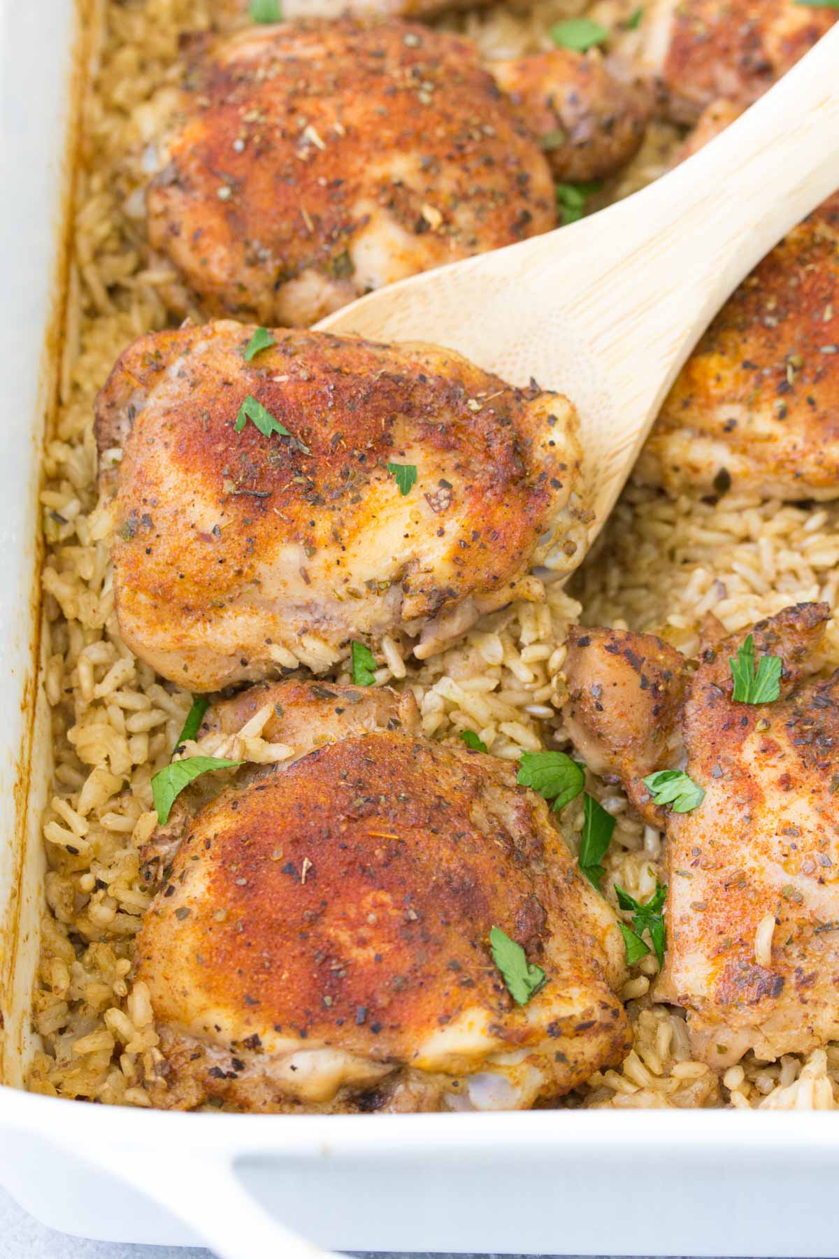 Baked chicken thighs and rice in baking dish with wooden spoon.