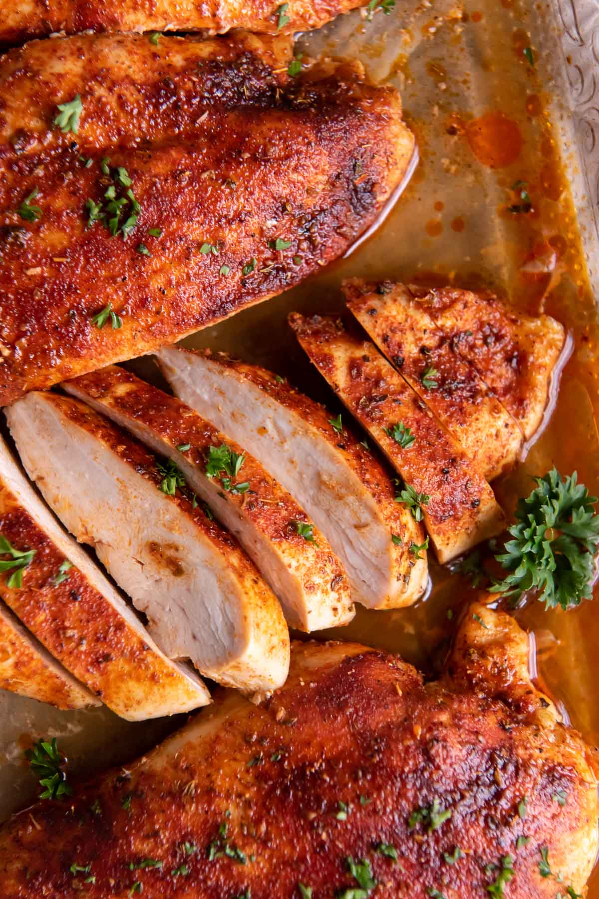 Sliced and unsliced baked chicken breast in baking dish.