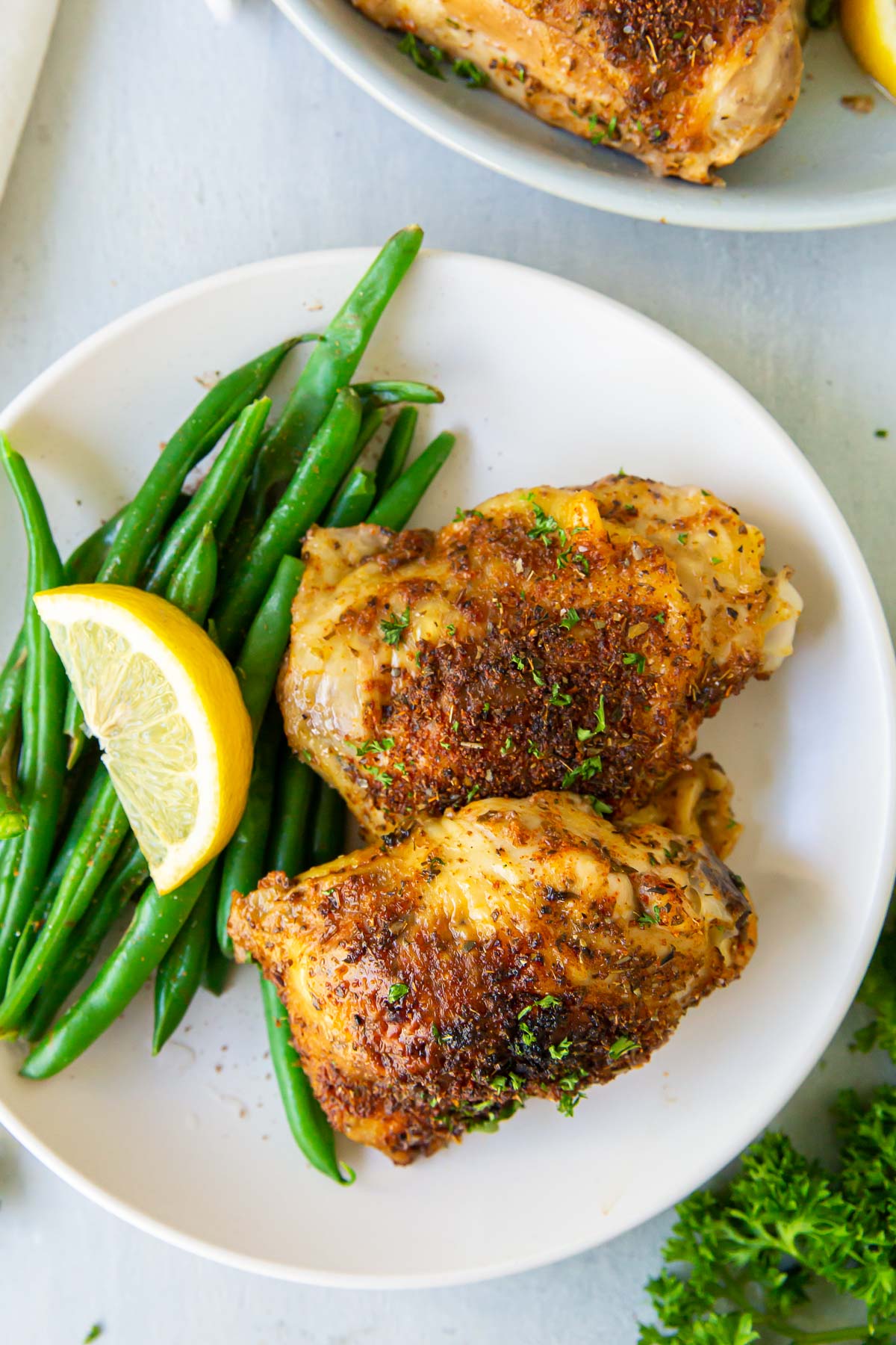Two baked chicken thighs served on a plate with green beans.