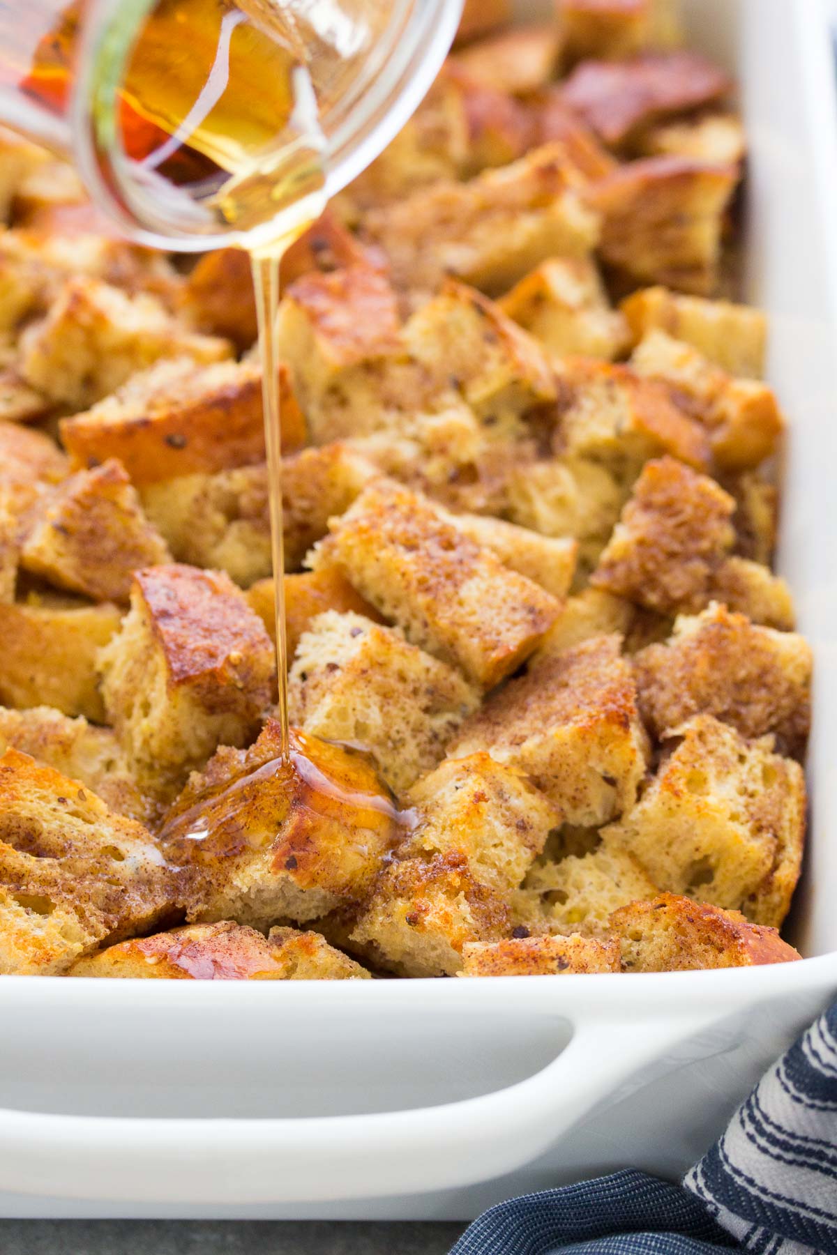 Pouring syrup over french toast casserole in baking dish.