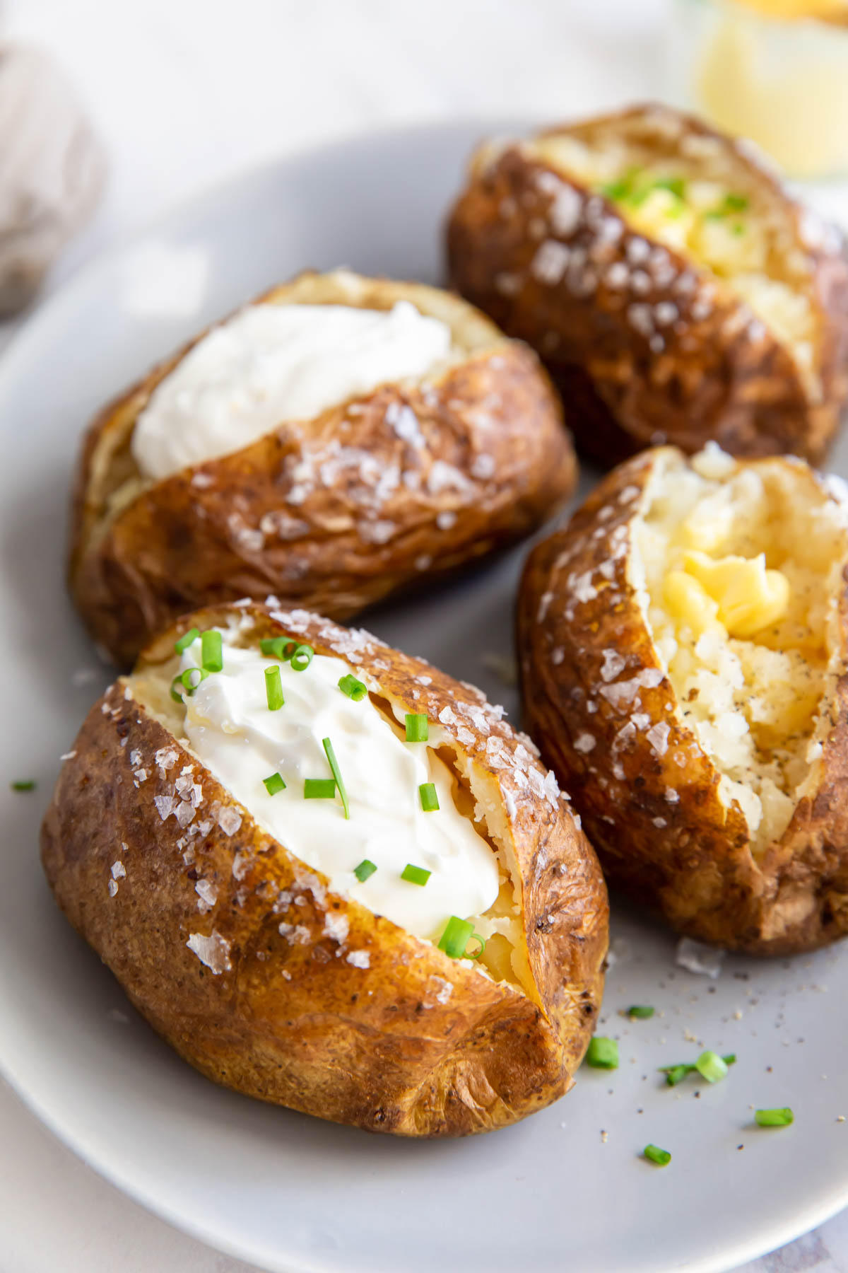 baked potatoes on a plate, some topped with butter and some with sour cream and chives