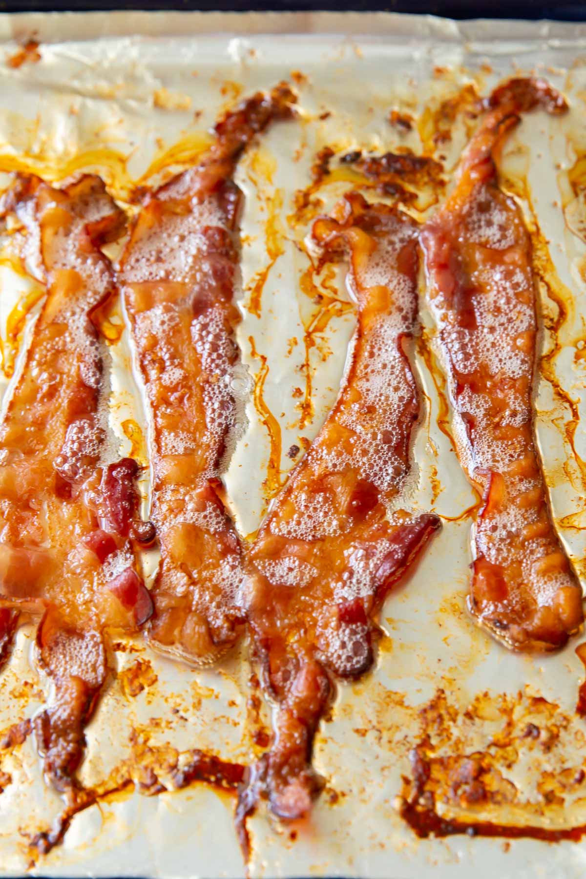 close up of four slices of baked bacon on a baking sheet