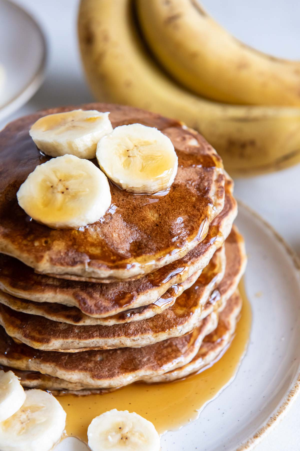 Stack of banana pancakes topped with banana slices and maple syrup.
