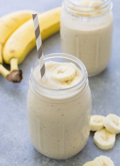 Banana smoothie in a glass with a straw and sliced bananas.
