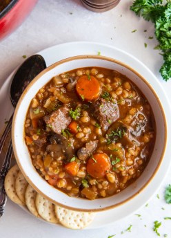 Bowl of beef barley soup with crackers on the side.