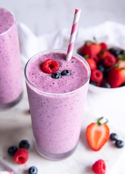 Berry smoothie in a tall glass garnished with fresh berries and a straw.
