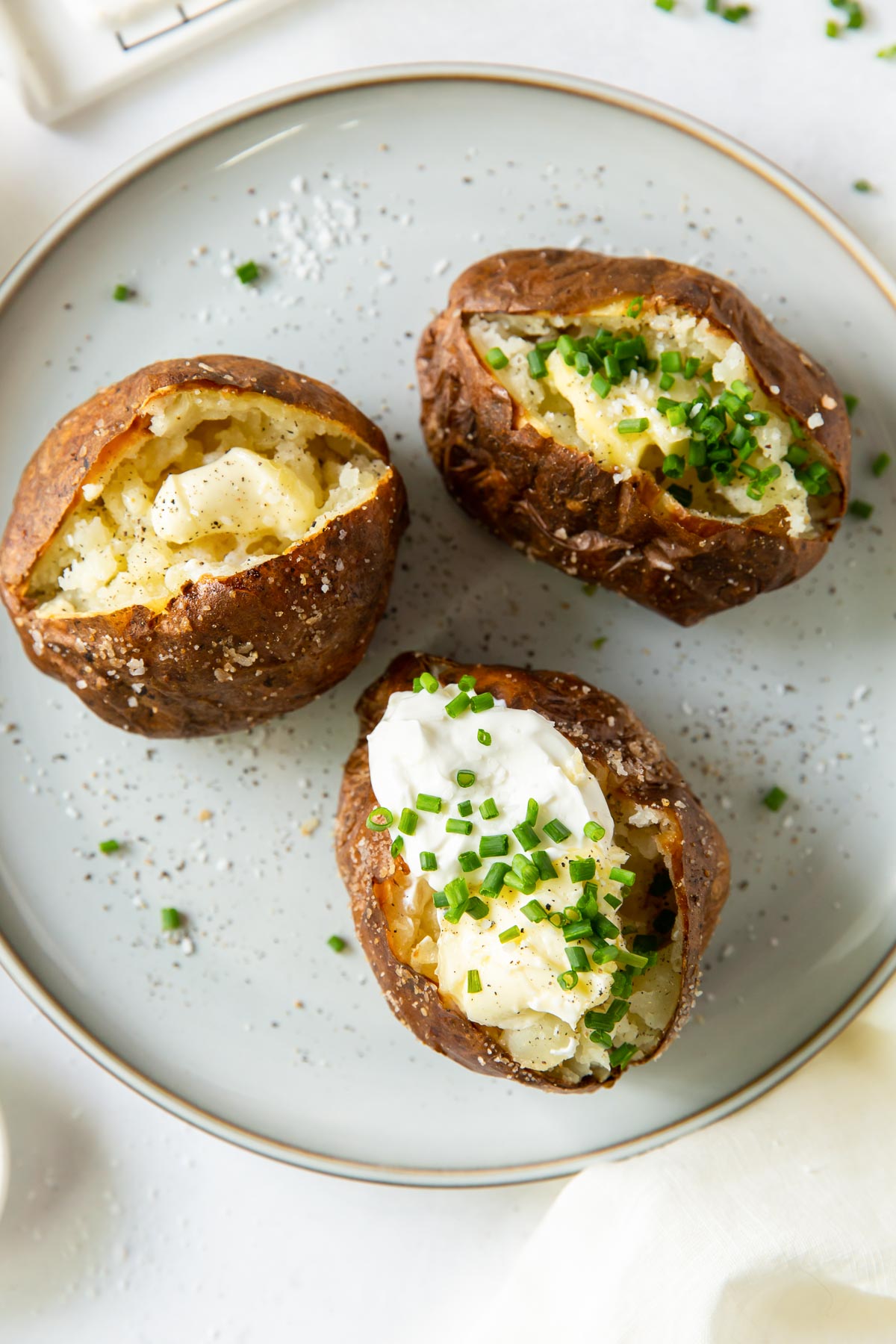 Three baked potatoes with toppings on a large plate.
