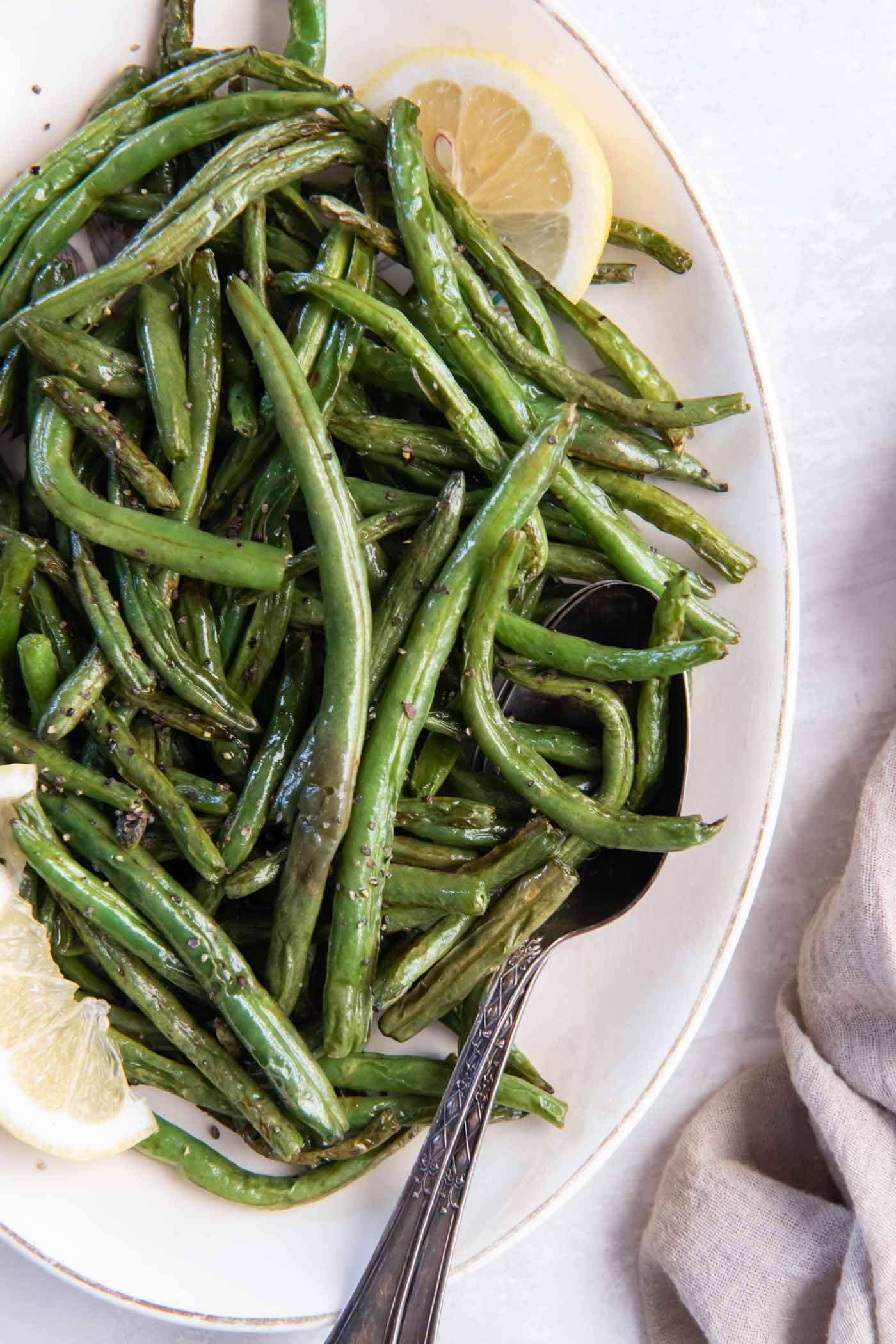 Air fryer green beans on serving dish with spoon and lemon slices.