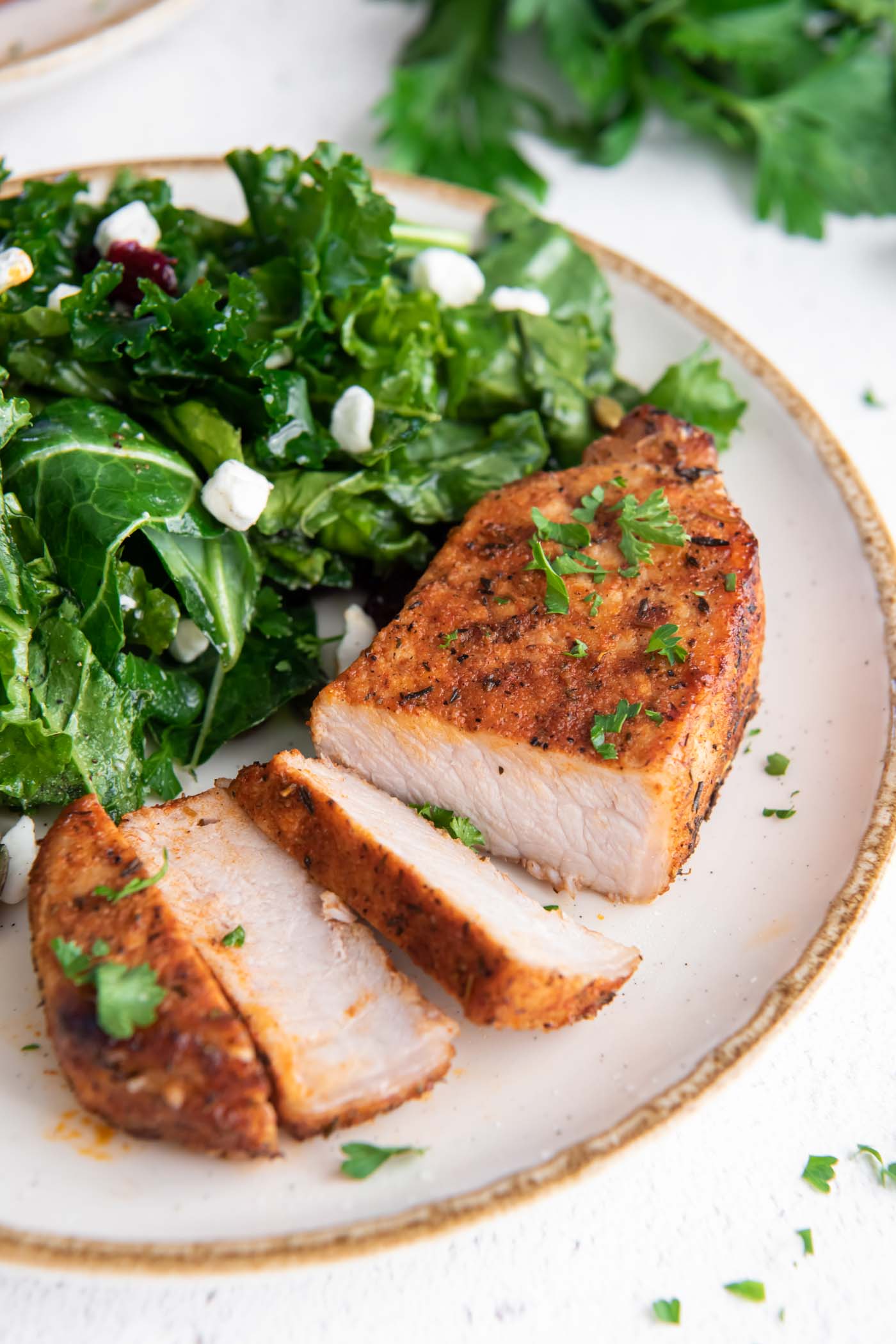 Partially sliced boneless pork chop on a plate served with kale salad.