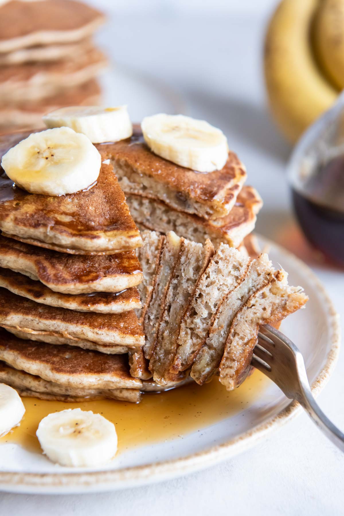 Stack of banana pancakes with bite on a fork.