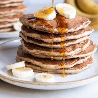 Stack of banana pancakes with maple syrup dripping down.
