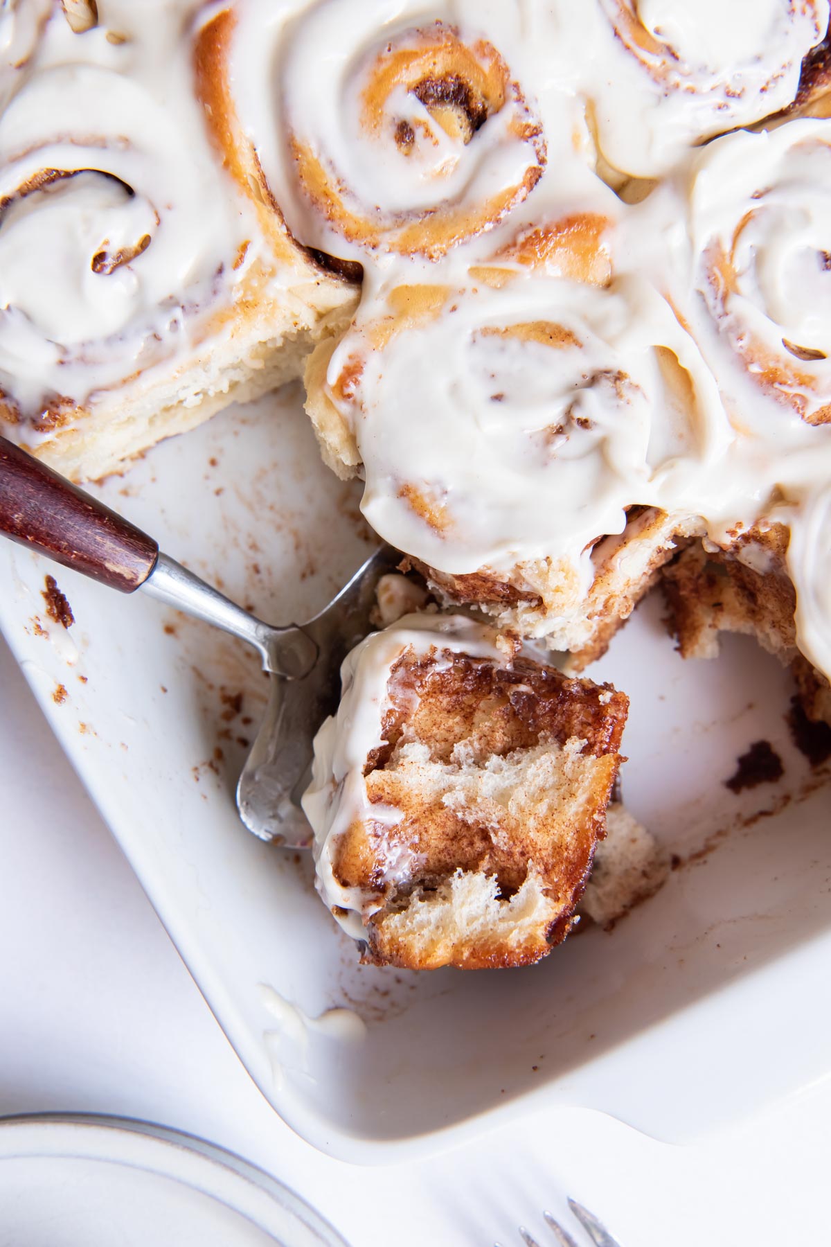 Cinnamon rolls in baking dish with a side view of cinnamon roll on a spatula.