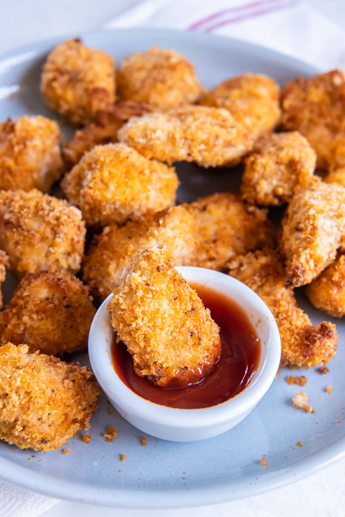 Air fryer chicken nuggets on a serving plate with one nugget in dish of ketchup.