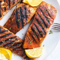 Close up of grilled salmon fillets on a plate with lemon wedges.