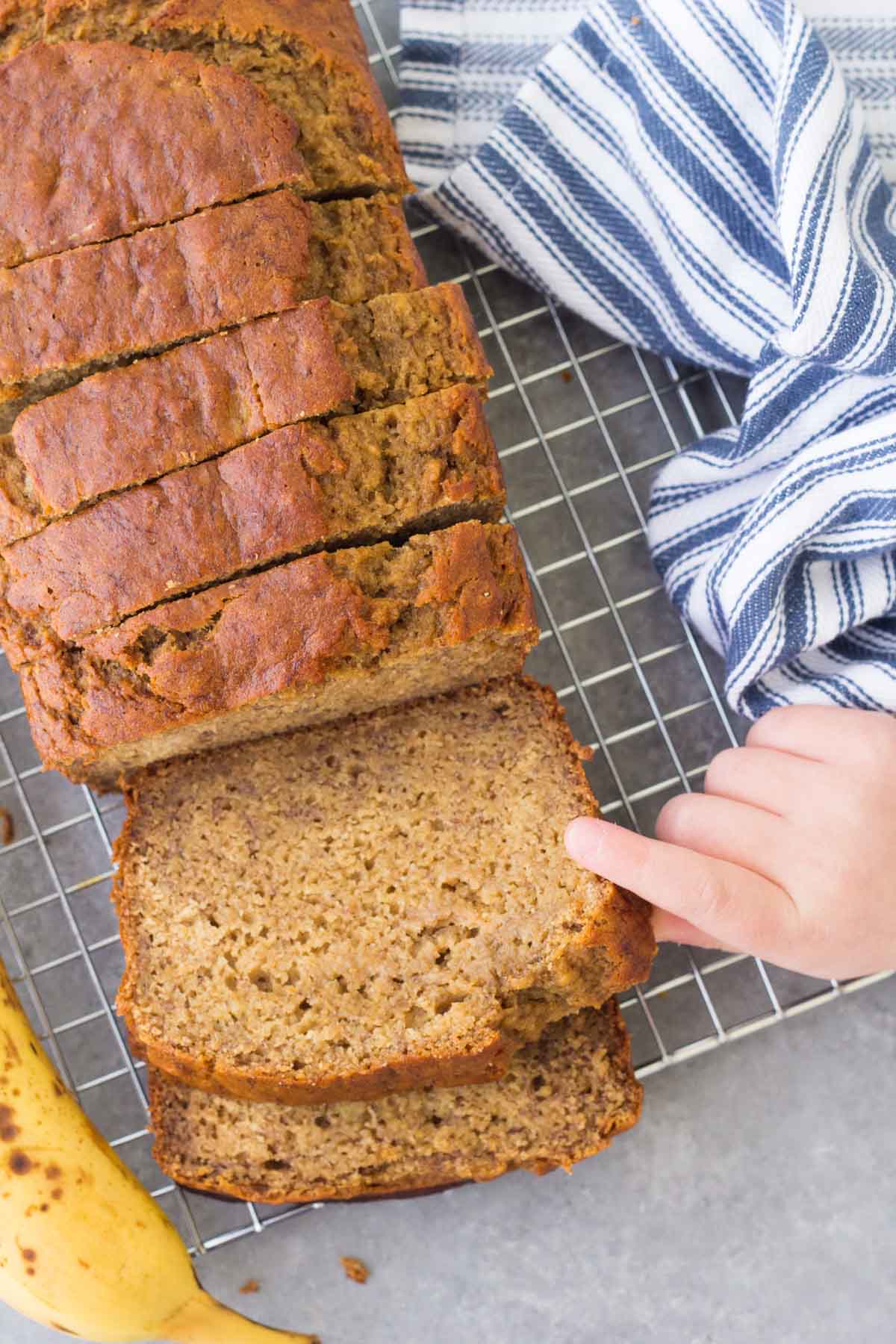 Child's hand grabbing a slice of healthy banana bread from the sliced loaf.