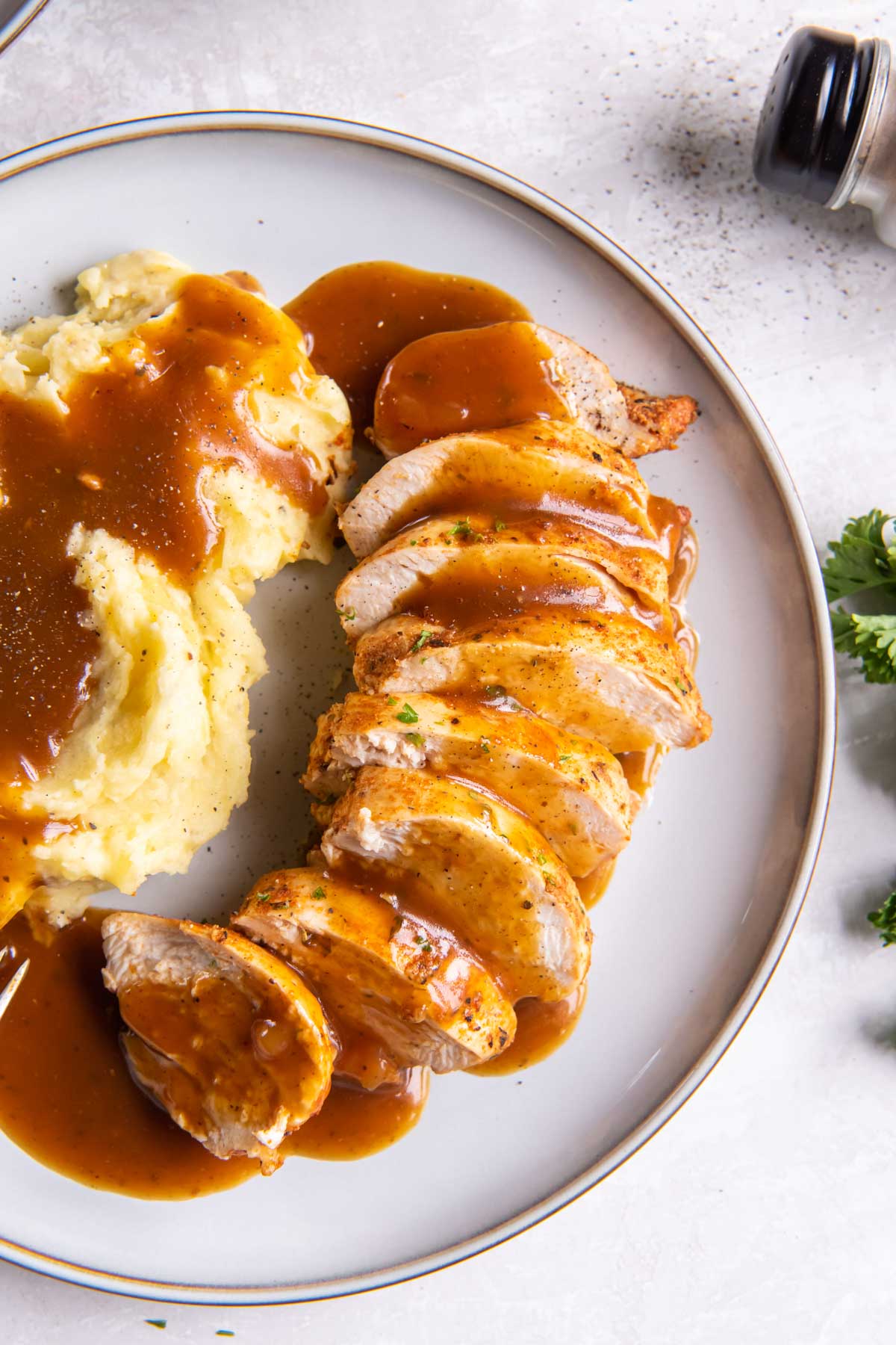 Sliced instant pot chicken breast drizzled with gravy with mashed potatoes on the side.