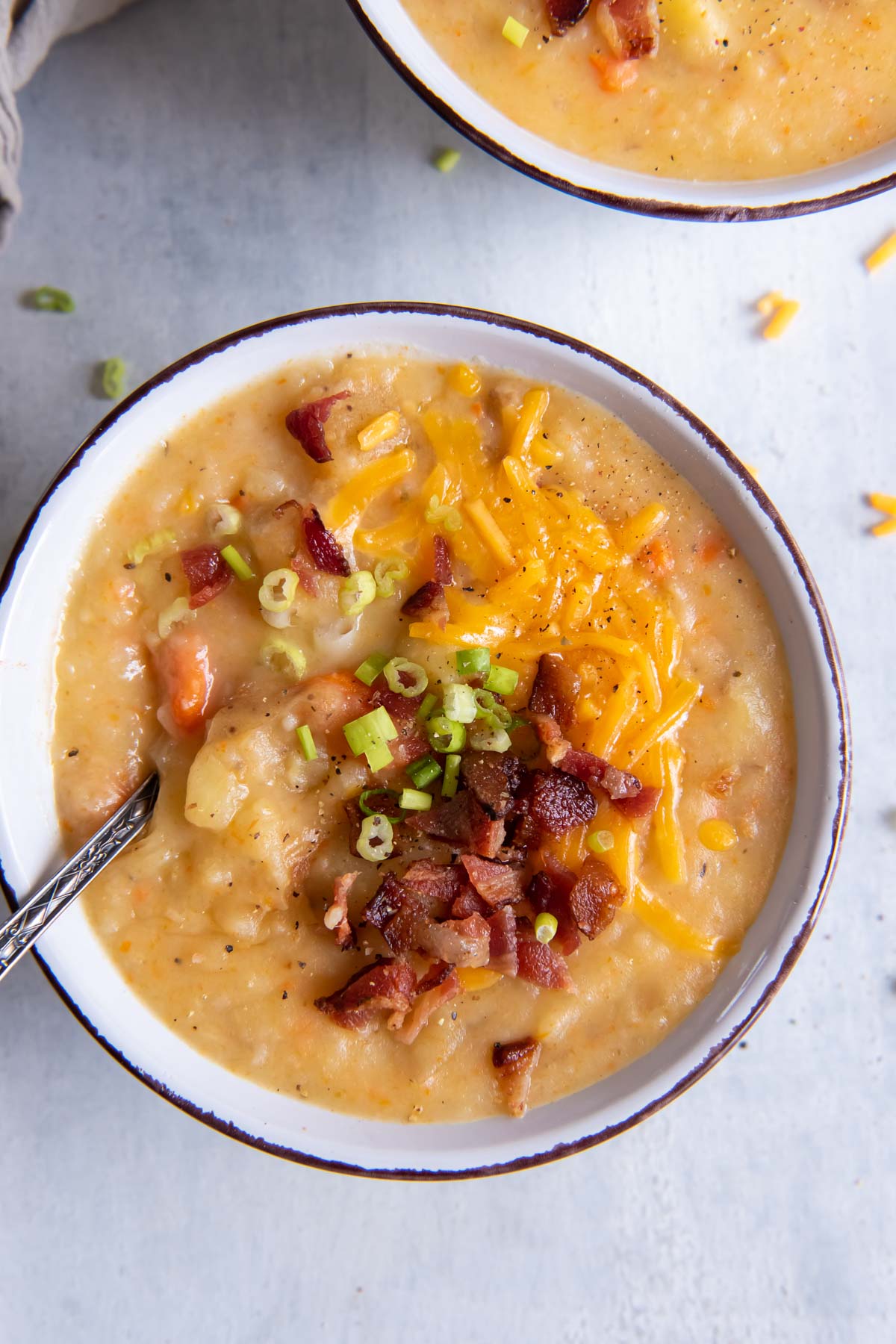 Instant pot potato soup served in a bowl with bacon, cheese, green onions and a spoon.