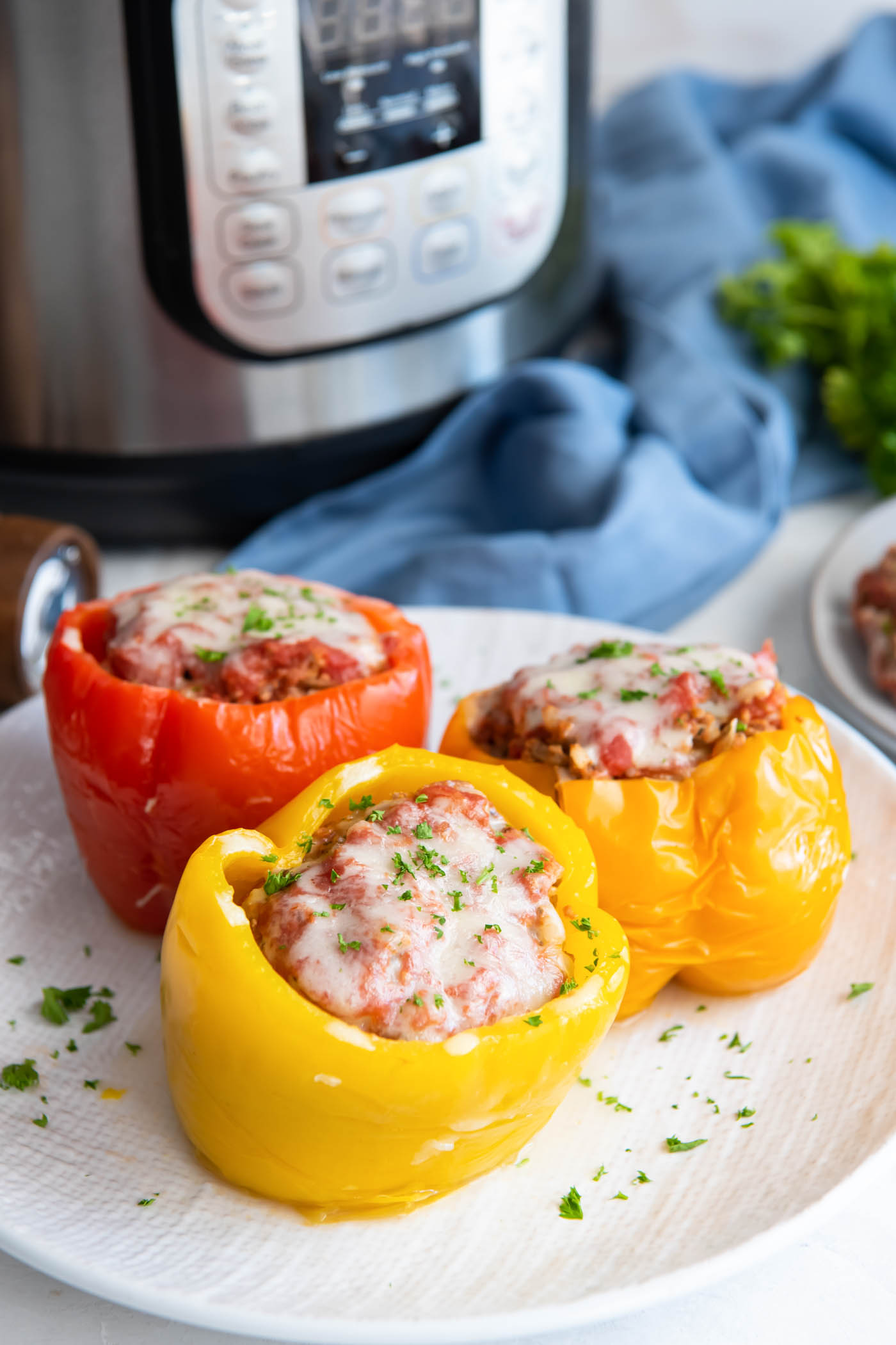 Three stuffed peppers on a plate with instant pot in the background.