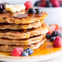Stack of five oatmeal pancakes topped with butter, maple syrup and fresh berries.