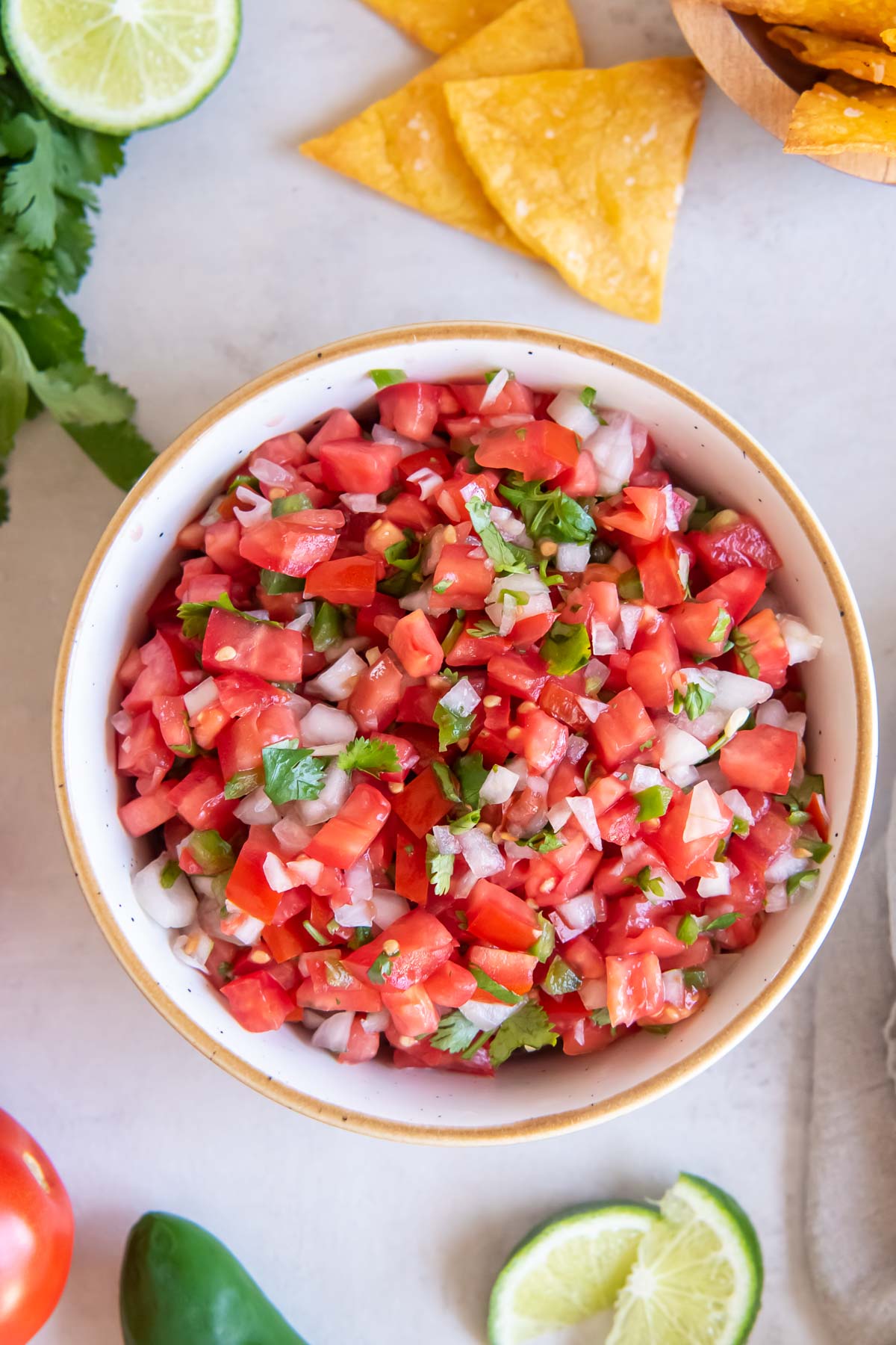 Bowl of pico de gallo with limes, cilantro and tortilla chips around it.