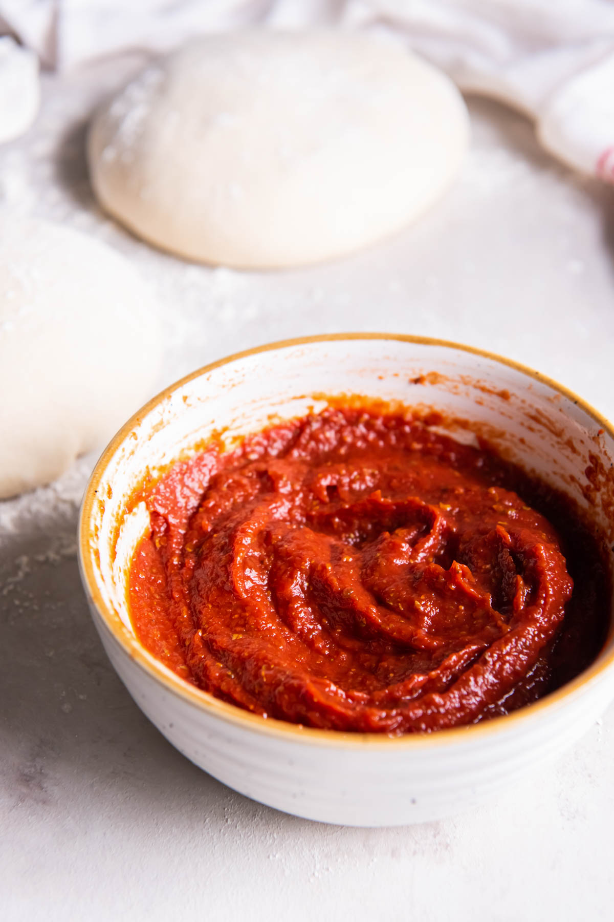 Pizza sauce in a bowl with two balls of pizza dough in background.