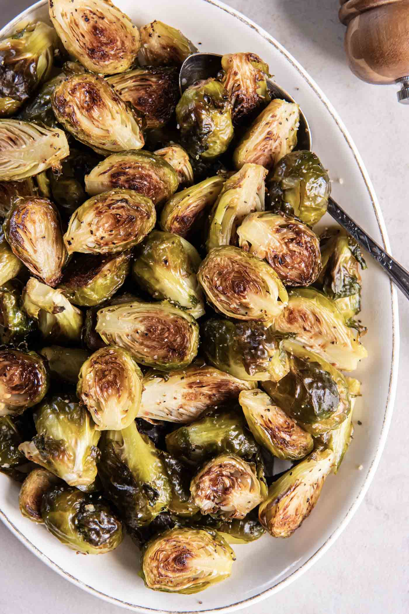 Roasted Brussels sprouts in an oval serving bowl with a serving spoon.