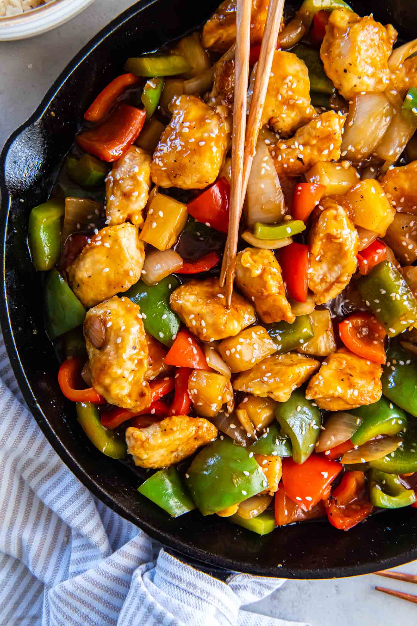 Sweet and sour chicken in a skillet with chopsticks.