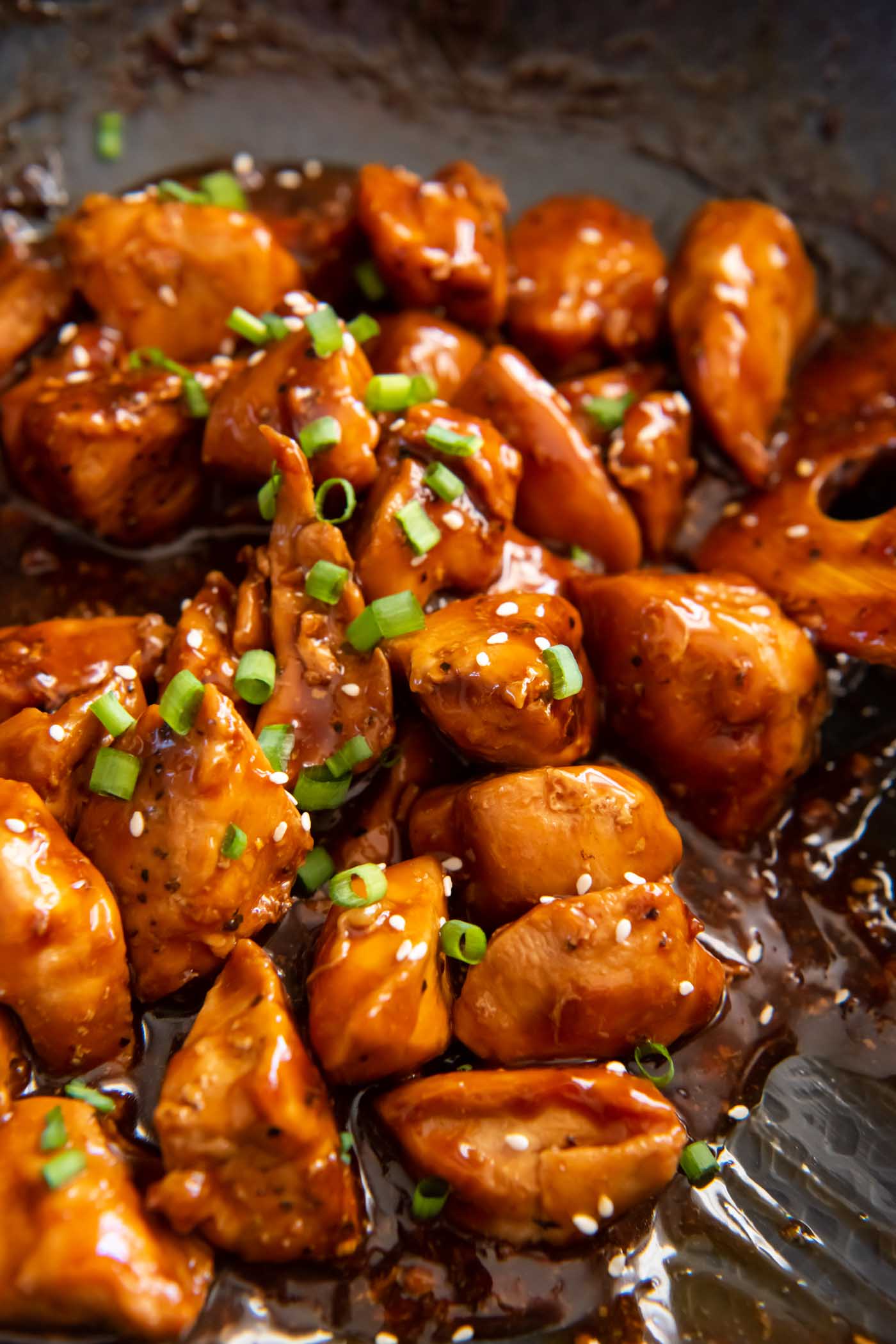 Close up of teriyaki chicken in a skillet garnished with sesame seeds and chopped green onions.