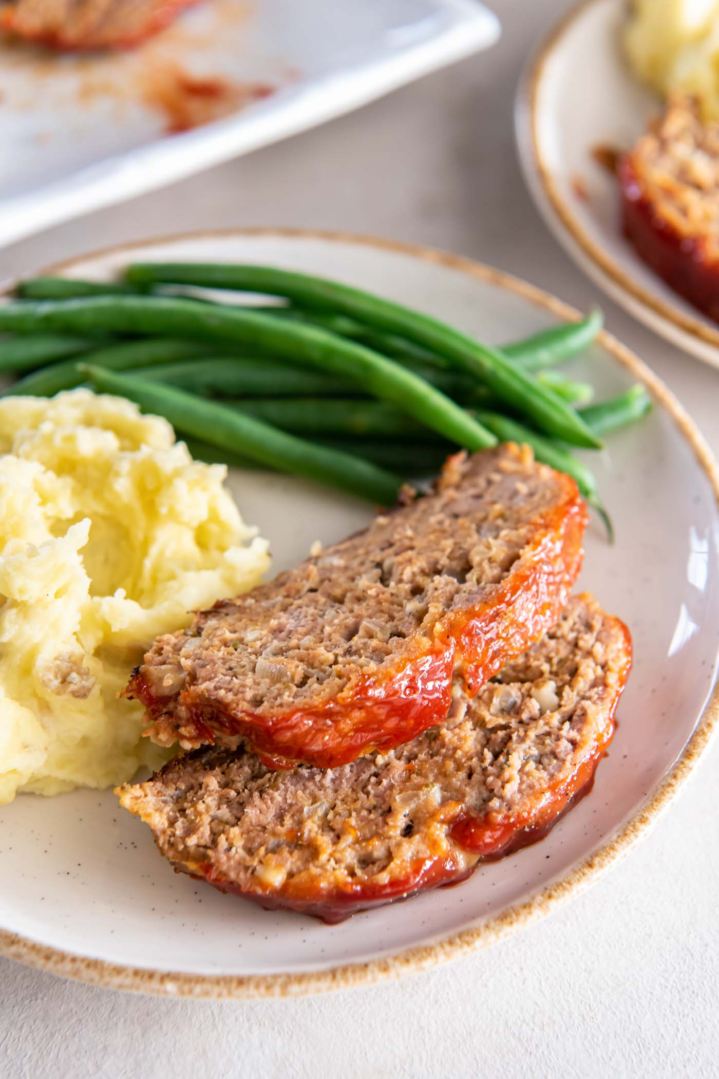 Two slices of turkey meatloaf, mashed potatoes and green beans on a plate.